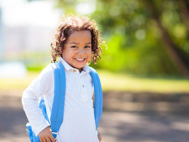 Little curly haired boy with blue backpack on the first day of new school year
