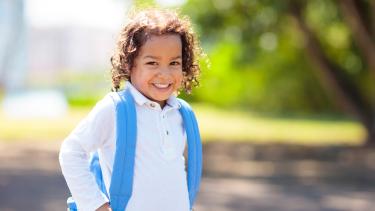 Little curly haired boy with blue backpack on the first day of new school year