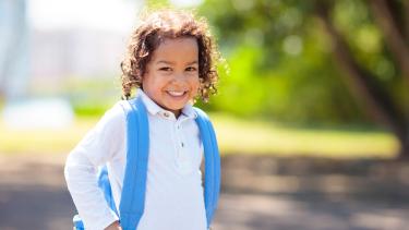 iStock - School Uniform Little curly haired boy with blue backpack on the first day of new school year