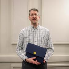 Male standing in front of wall holding certificate